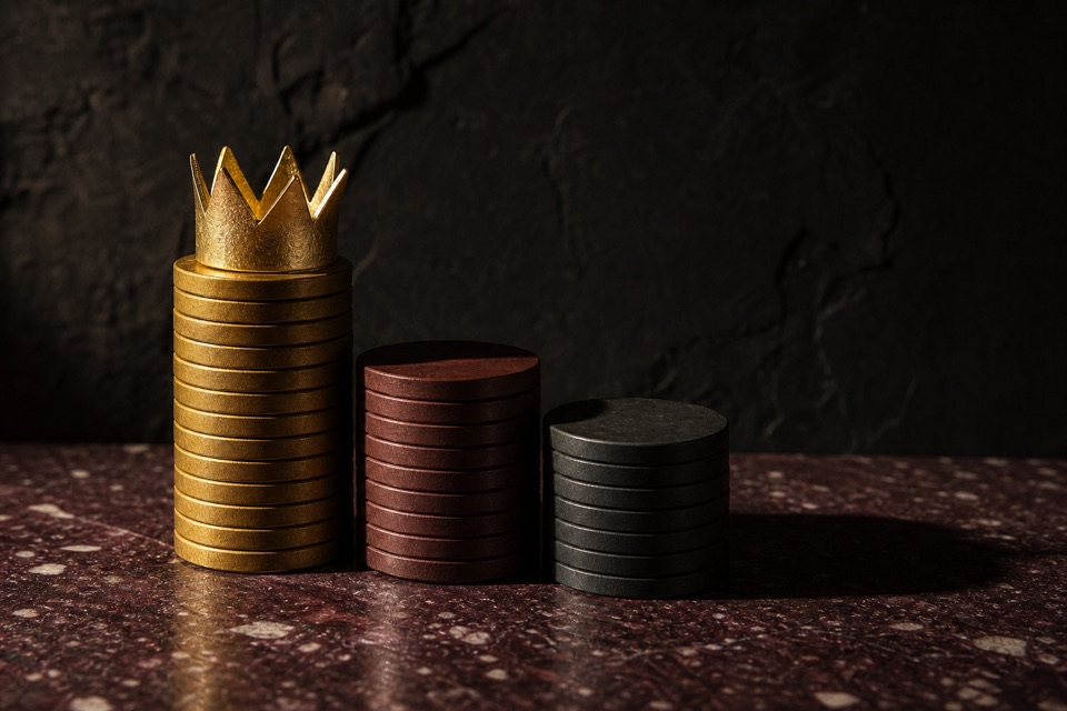 Eine goldene Krone auf einem Stapel Spieljetons neben zwei weiteren Jetonstapeln auf einer Porphyrplatte